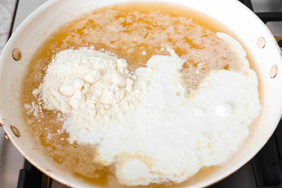 Overhead shot of flour mixture with cream chicken broth and parmesan cheese in a skillet. 