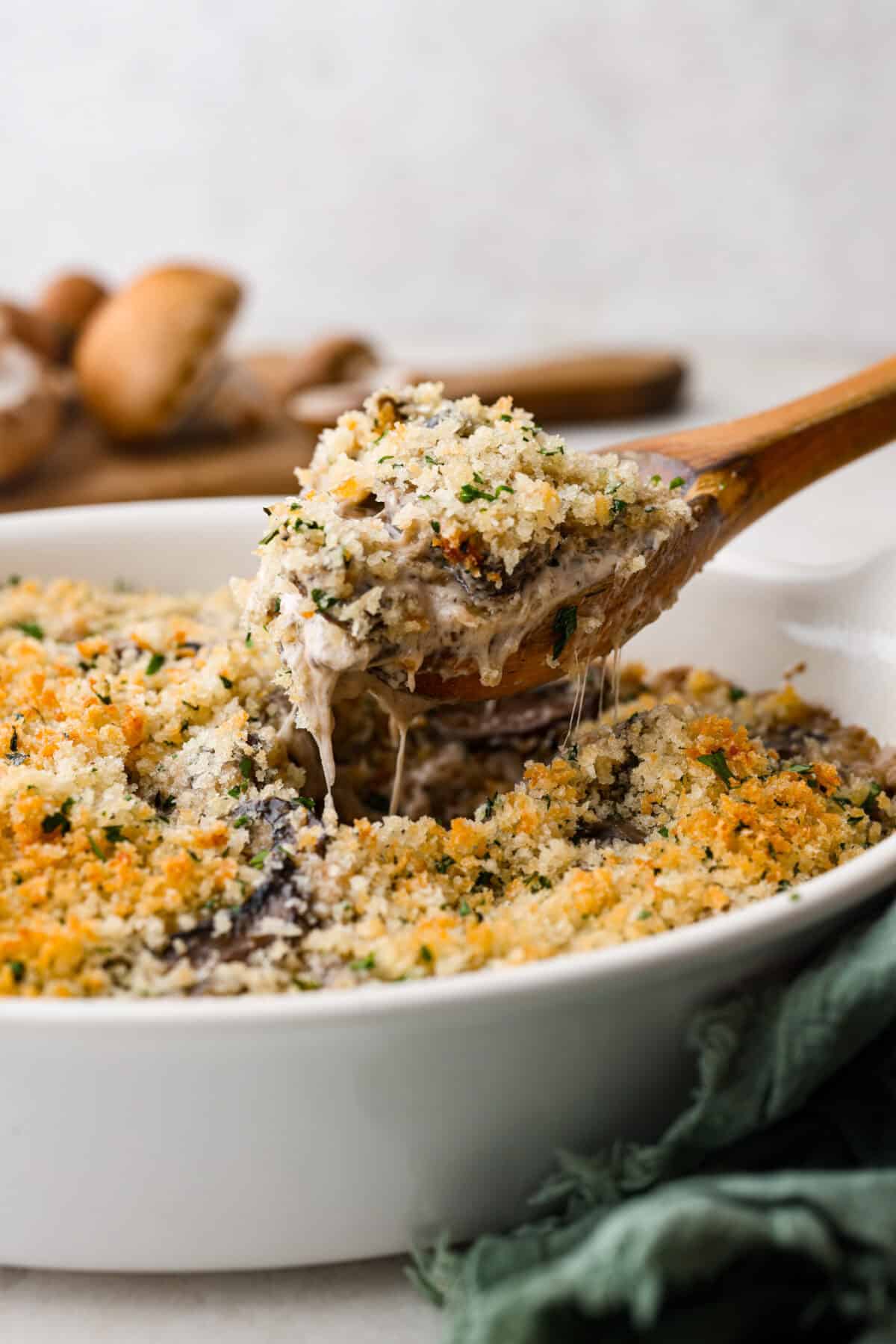 Close side view of a wood spoon lifting up mushroom casserole from the baking dish.