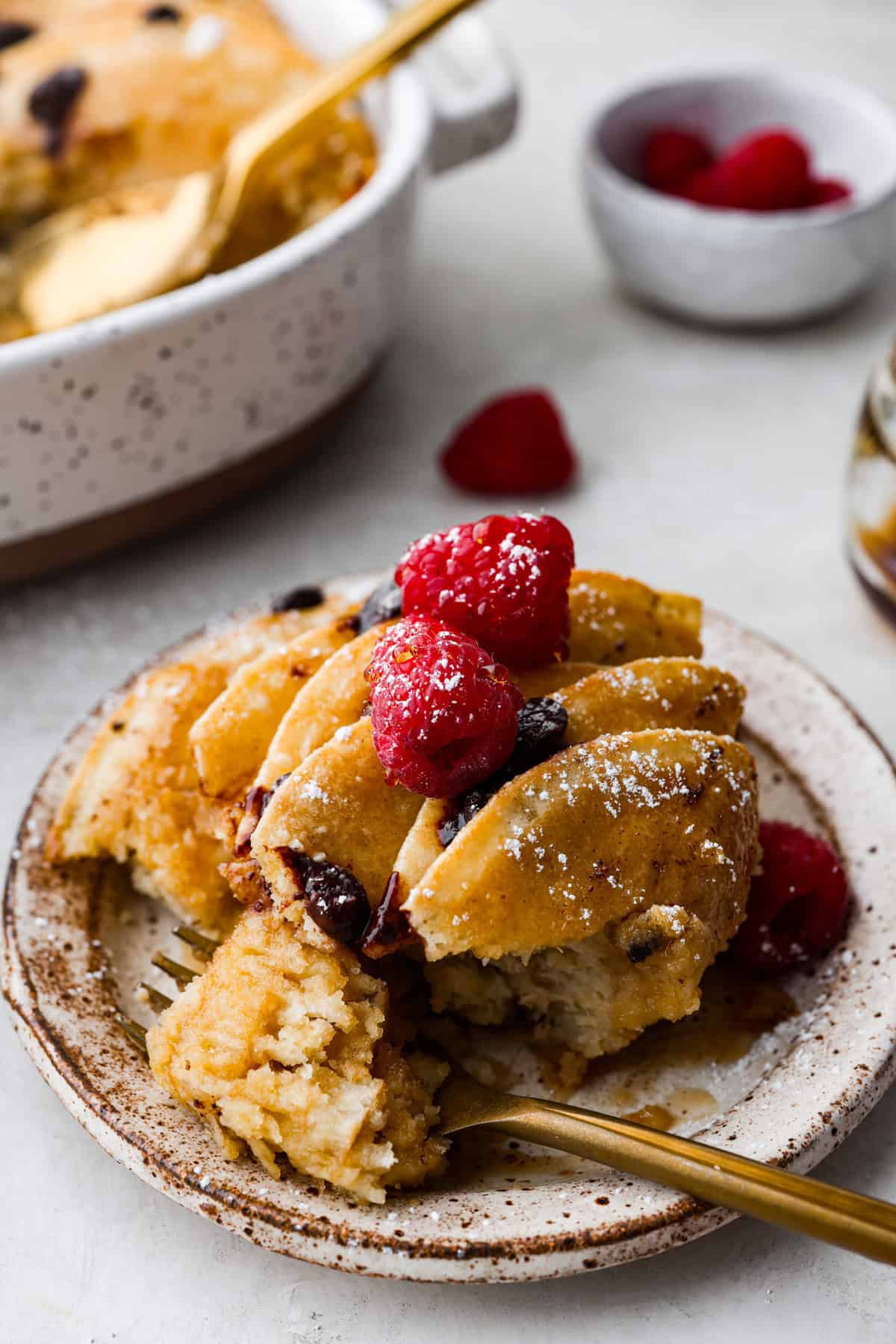 Pancake Casserole is a fun new Christmas or Easter breakfast idea. It has lots of buttery pancakes soaked overnight in a creamy custard, is baked to perfection, and served with your favorite toppings! Angle shot of plated casserole with berries on top.