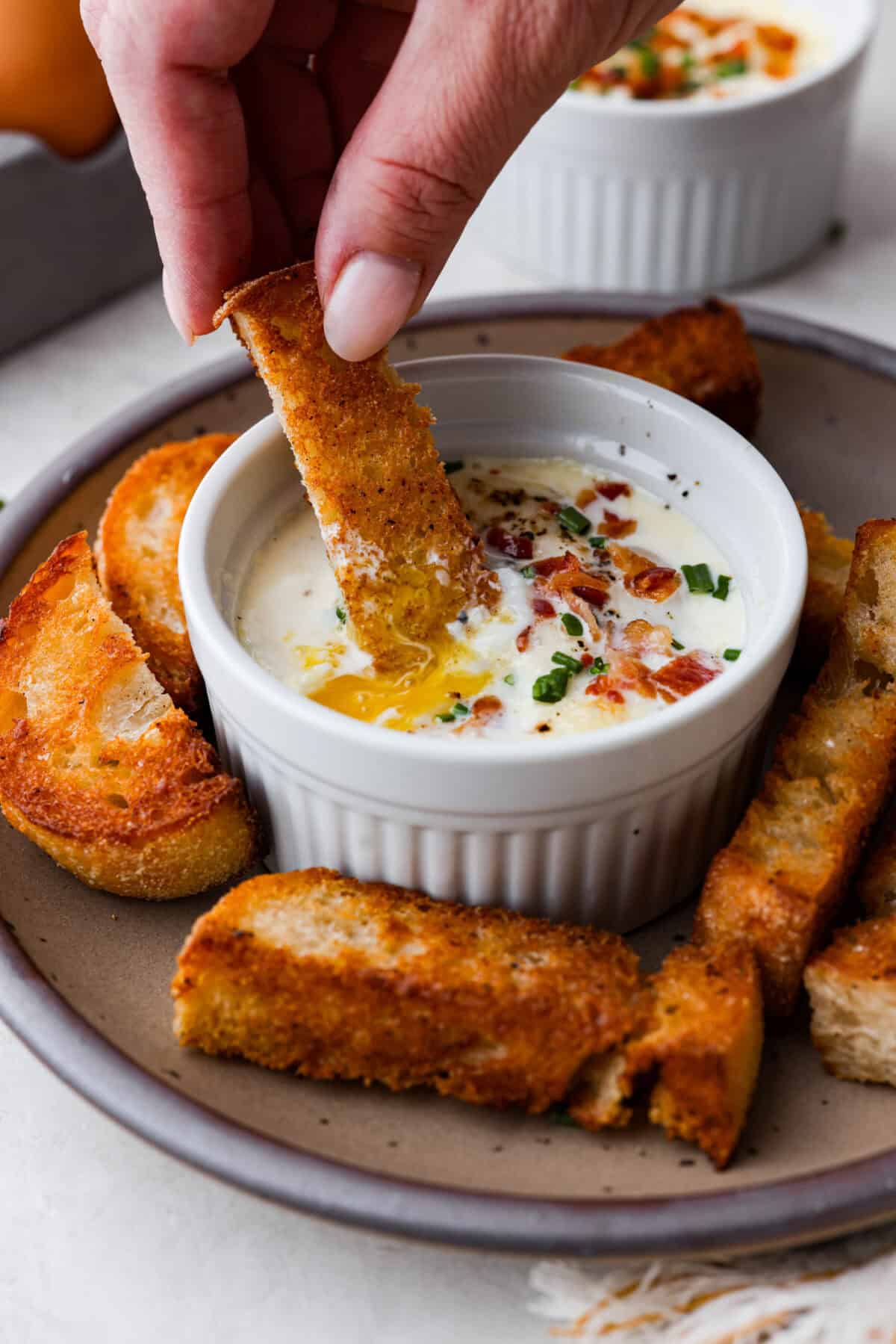 Side shot of someone dipping a crostini in shirred eggs.