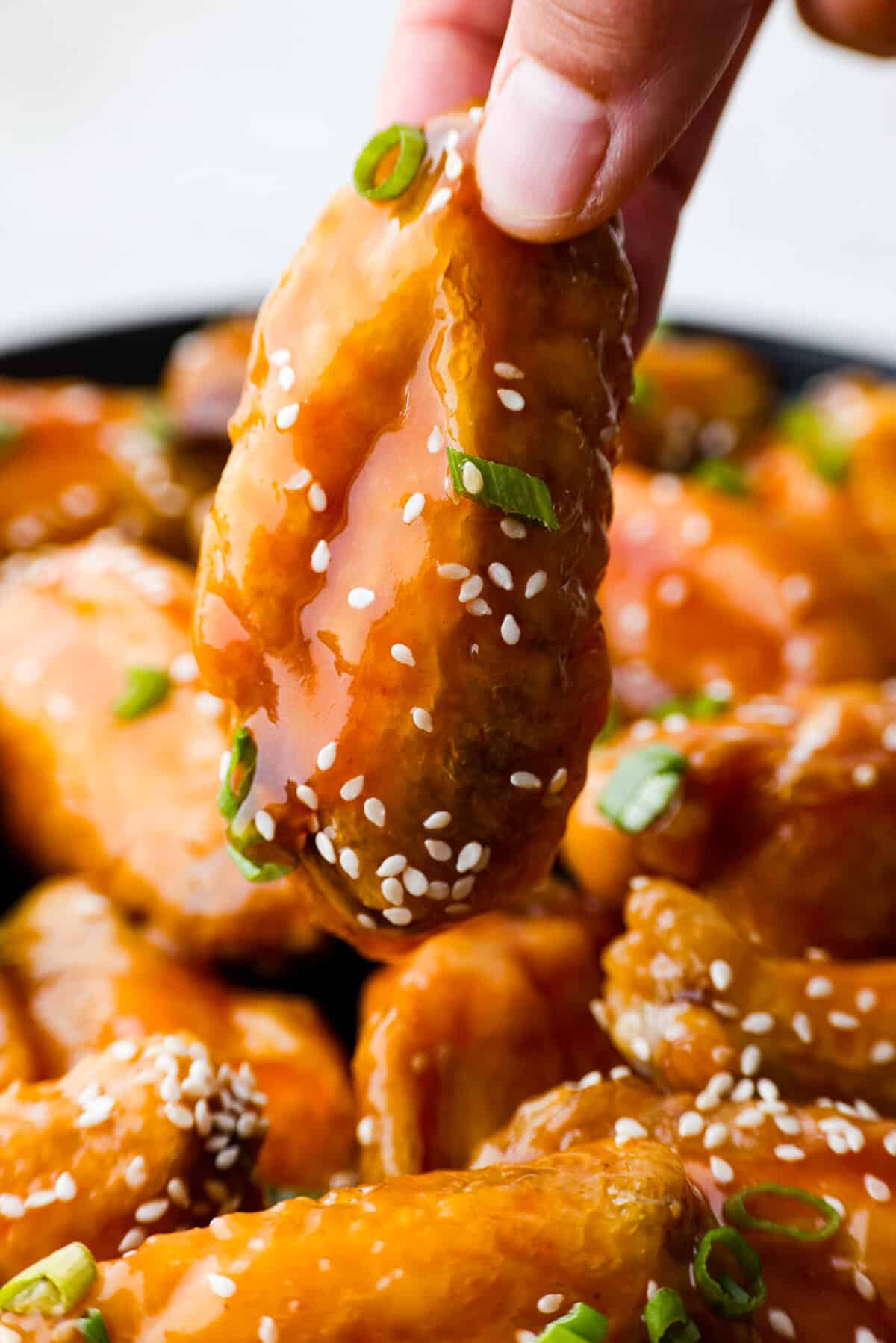 These sweet and sour wings are the perfect appetizer to serve for your next party, game day, or after-school snack. They are baked to crispy perfection and then doused in a sticky, sweet, and sour sauce. Close up shot of sweet and sour wing being lifted off the platter.