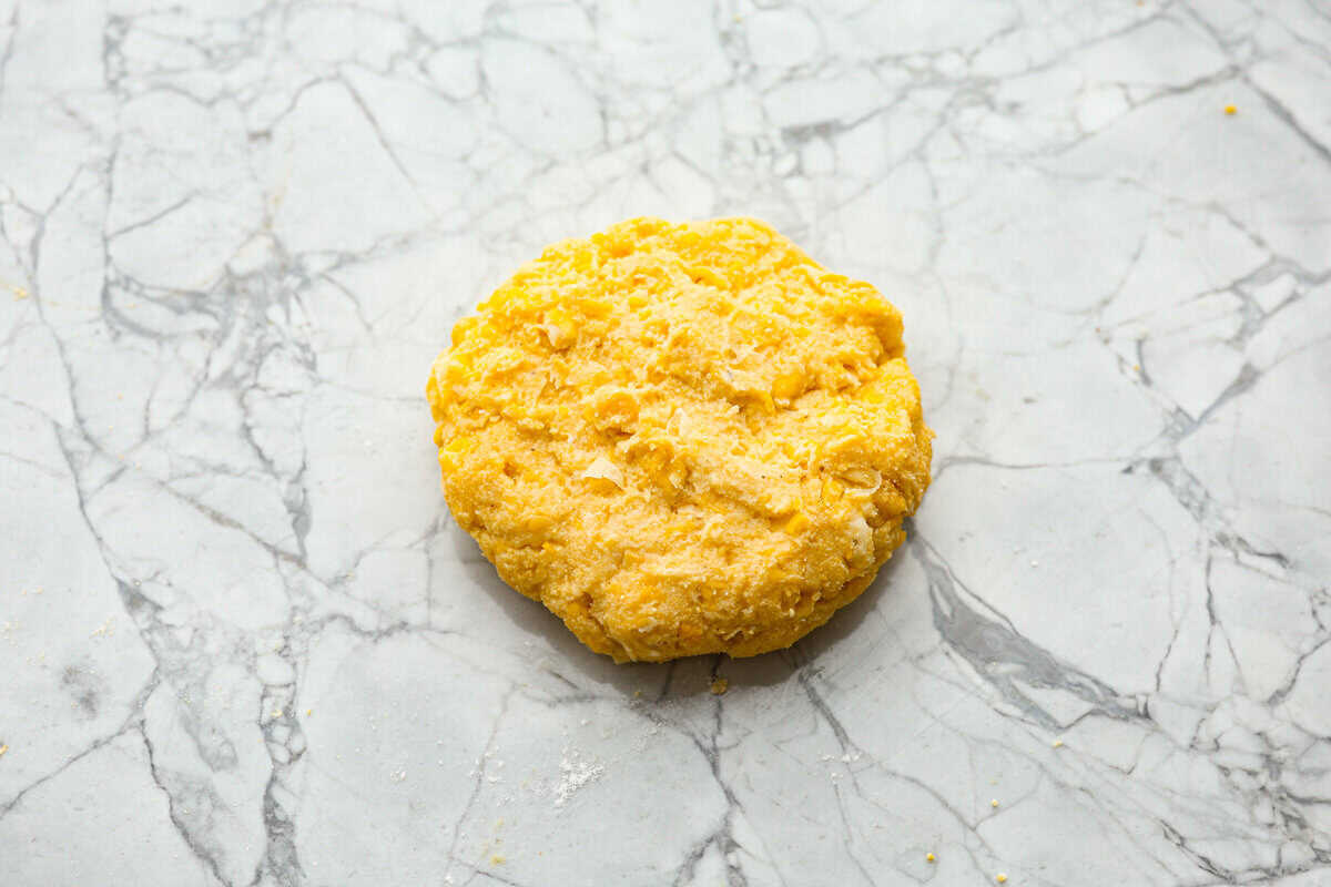 Homemade Sweet Corn Tamale Cakes are an explosion of delicious flavor in every bite! With this easy recipe you can bring this Cheesecake Factory favorite right to your own kitchen. Add the signature topping to really take these to the next level! Overhead shot of formed corn cake on a counter top.