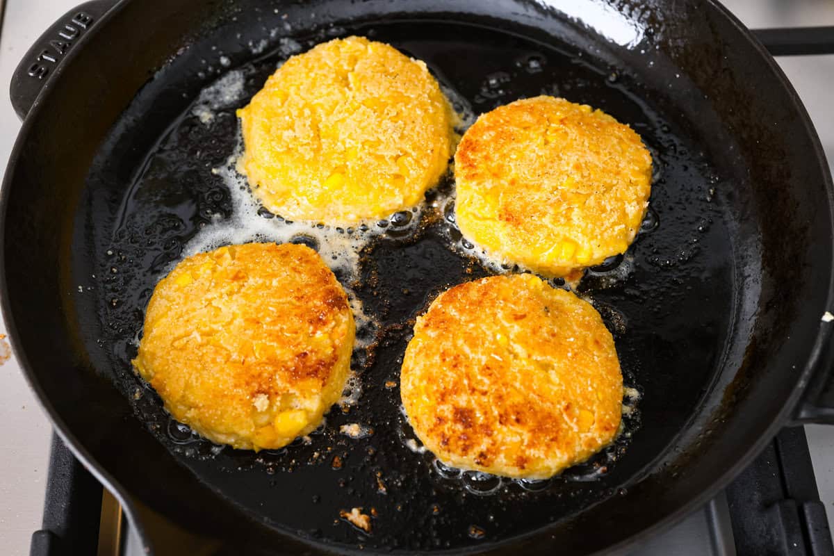 Homemade Sweet Corn Tamale Cakes are an explosion of delicious flavor in every bite! With this easy recipe you can bring this Cheesecake Factory favorite right to your own kitchen. Add the signature topping to really take these to the next level! Overhead shot of corn cakes frying in oil on a skillet.