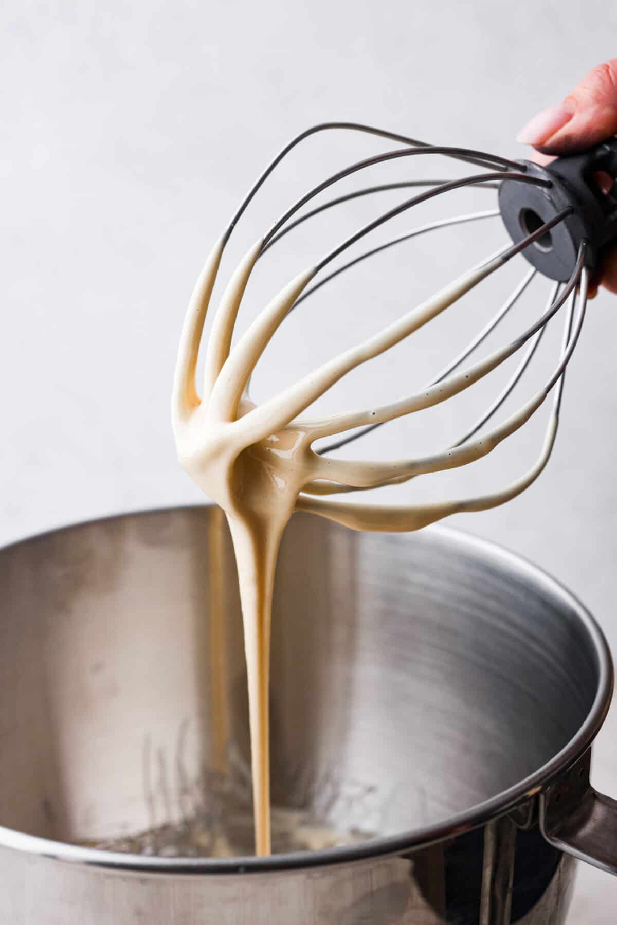 Close up shot of a whisk attachment of a stand mixer dripping with creamed honey. 