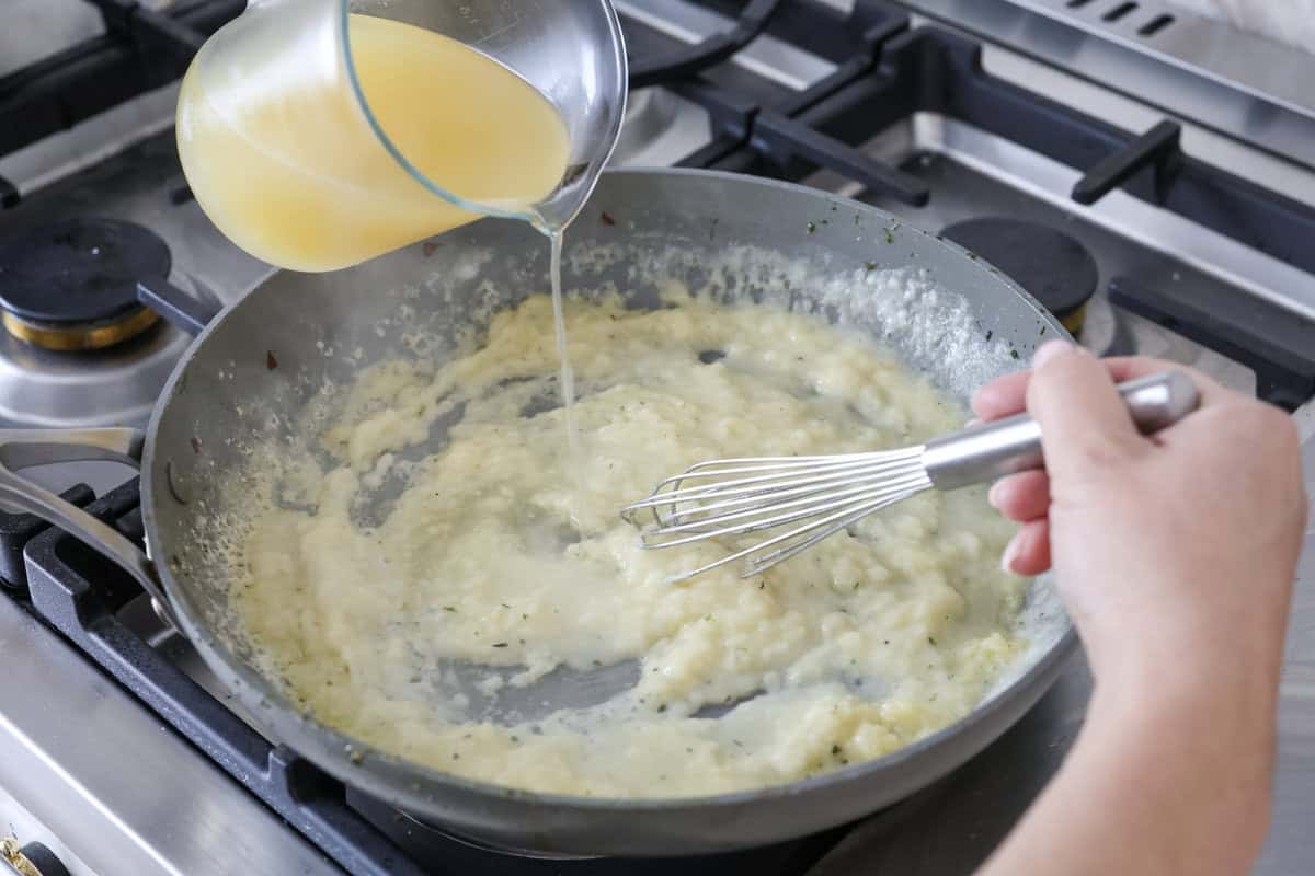 Chicken pot pie casserole is a fun twist on the classic pot pie. It's made with buttery biscuit dough, tender chicken, crunchy veggies, and the most delicious creamy sauce loaded with incredible seasoning. Comfort food at its finest! Angle shot of someone pouring the chicken broth, half and half, and lemon juice in the the butter and flour mixture.