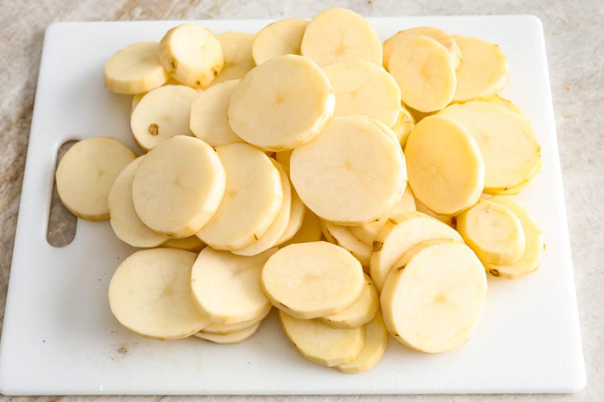 Overhead shot of a pile of thinly sliced potatoes on a cutting board.