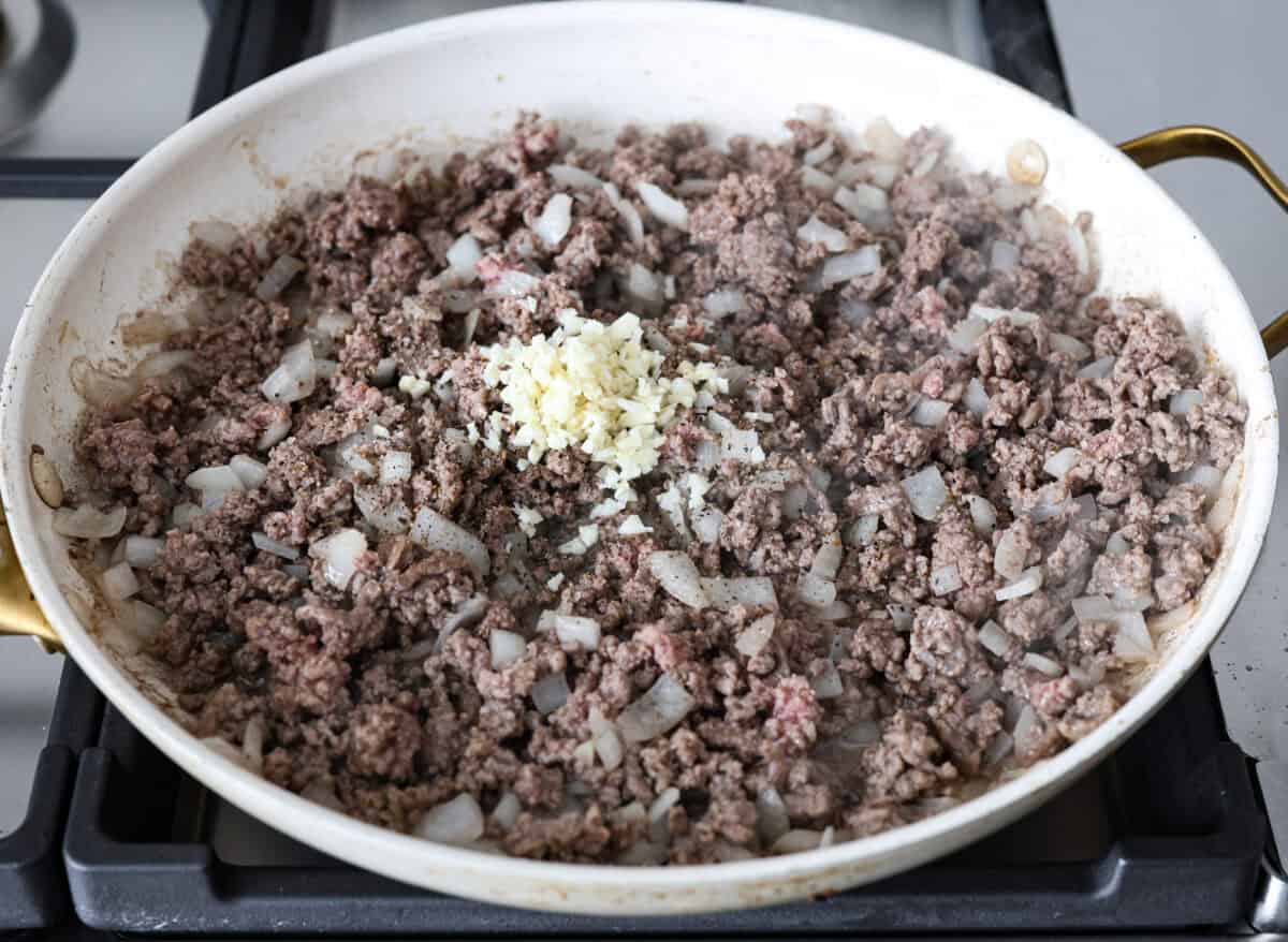 Angle shot of cooked ground beef and onions in a skillet with garlic and seasonings over the top. 