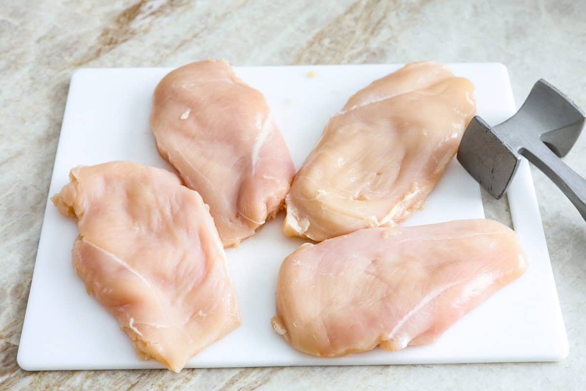 Skillet chicken cordon bleu is one of those recipes my whole family loves. You can't beat the creamy sauce, crispy chicken, and smokey ham, all covered in melty Swiss cheese. Overhead shot of chicken breasts on a cutting board with meat tenderizer next to them.