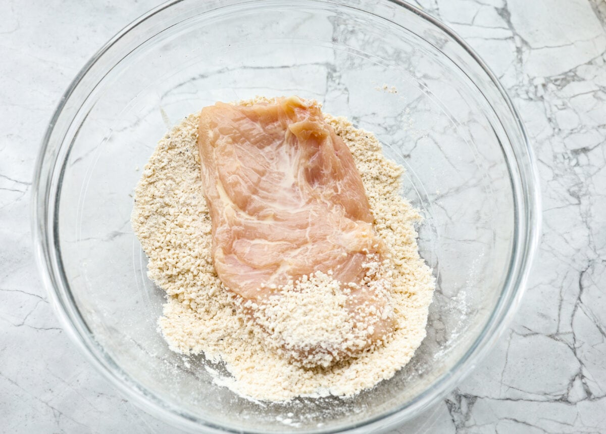 Overhead shot of a tenderized chicken breast in the bowl of the breadcrumb mixture. 