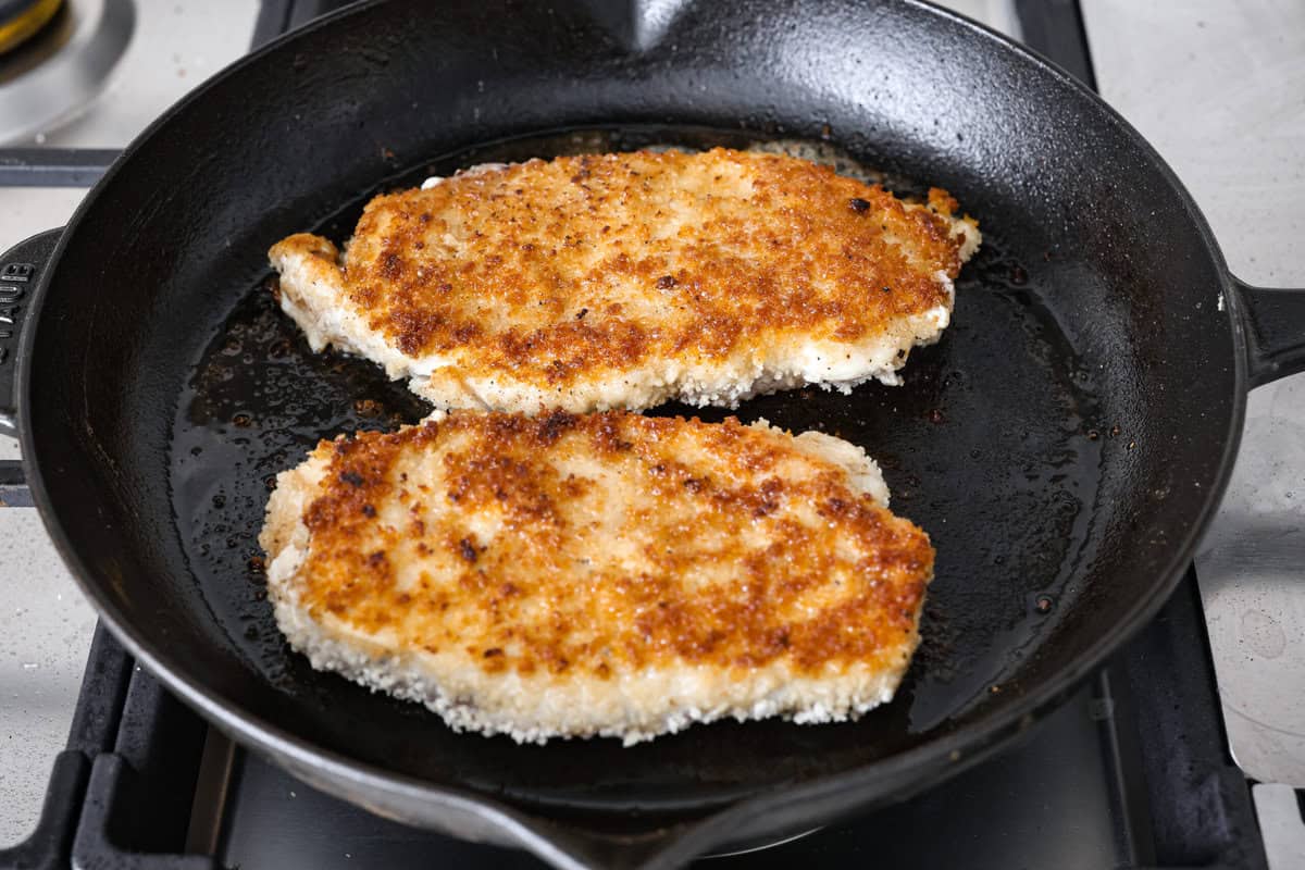 Skillet chicken cordon bleu is one of those recipes my whole family loves. You can't beat the creamy sauce, crispy chicken, and smokey ham, all covered in melty Swiss cheese. Angle shot of the chicken breast frying in the hot oil in the skillet.