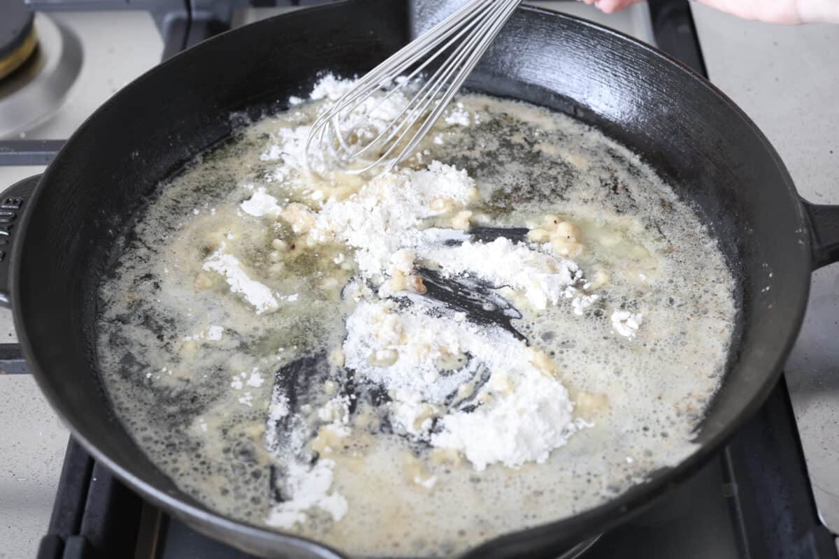 Angle shot of someone whisking the flour into the melted butter in a skillet. 