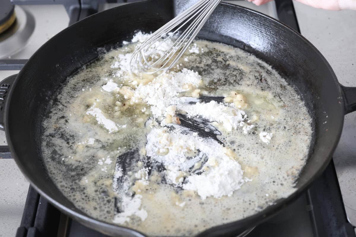 Skillet chicken cordon bleu is one of those recipes my whole family loves. You can't beat the creamy sauce, crispy chicken, and smokey ham, all covered in melty Swiss cheese. Angle shot of someone whisking the flour into the melted butter in a skillet.