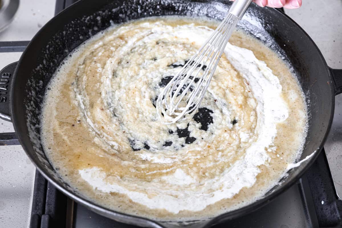 Skillet chicken cordon bleu is one of those recipes my whole family loves. You can't beat the creamy sauce, crispy chicken, and smokey ham, all covered in melty Swiss cheese. Angle shot of someone slowly adding in the chicken broth and cream mixture into the butter and flour mixture whisking continually.