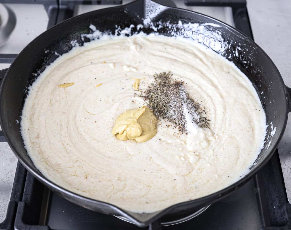 Skillet chicken cordon bleu is one of those recipes my whole family loves. You can't beat the creamy sauce, crispy chicken, and smokey ham, all covered in melty Swiss cheese. Angle shot of the dijon mustard and seasonings on top of the sauce in the skillet.