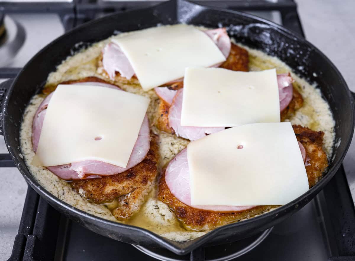 Skillet chicken cordon bleu is one of those recipes my whole family loves. You can't beat the creamy sauce, crispy chicken, and smokey ham, all covered in melty Swiss cheese. Angle shot of the crispy chicken breasts covered in ham and cheese in the skillet with the sauce.