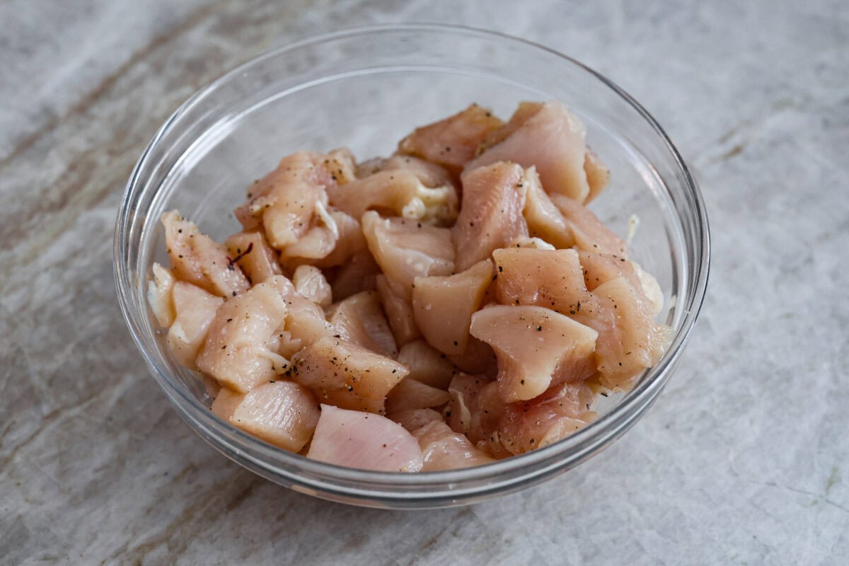 Angle shot of seasoned, cubed raw chicken in a bowl. 