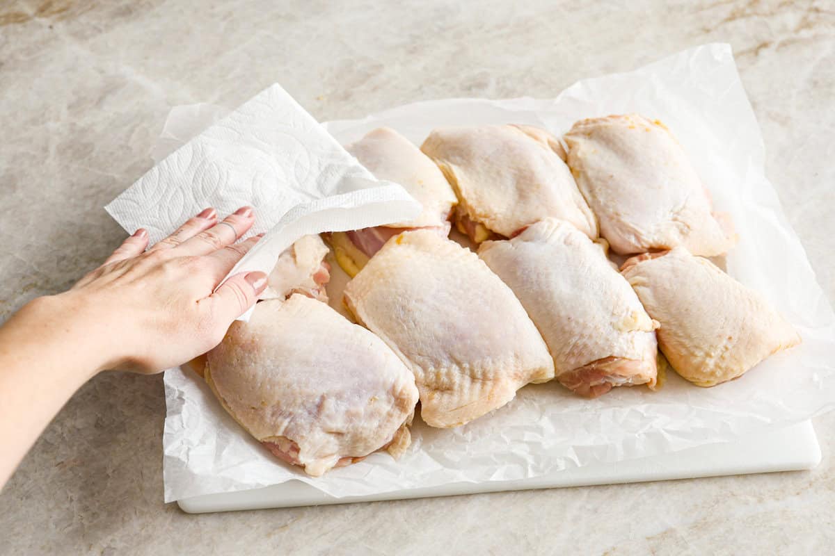 Miso chicken is super delicious and perfect for fans of bold Asian flavor. The skin crisps up, the meat stays juicy and tender, and the glaze caramelizes, creating a savory sauce perfect for drizzling over rice. Angle shot of someone drying off the chicken thighs with a paper towel.