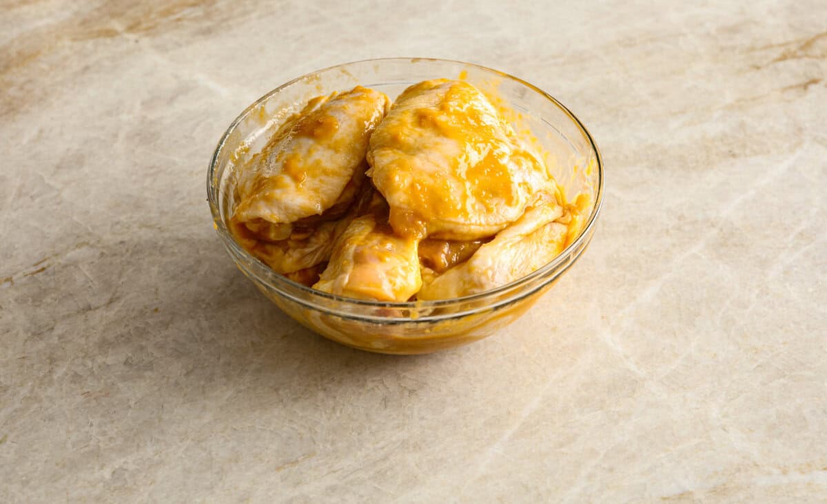 Miso chicken is super delicious and perfect for fans of bold Asian flavor. The skin crisps up, the meat stays juicy and tender, and the glaze caramelizes, creating a savory sauce perfect for drizzling over rice. Angle shot of chicken thighs doused in sauce in a bowl.