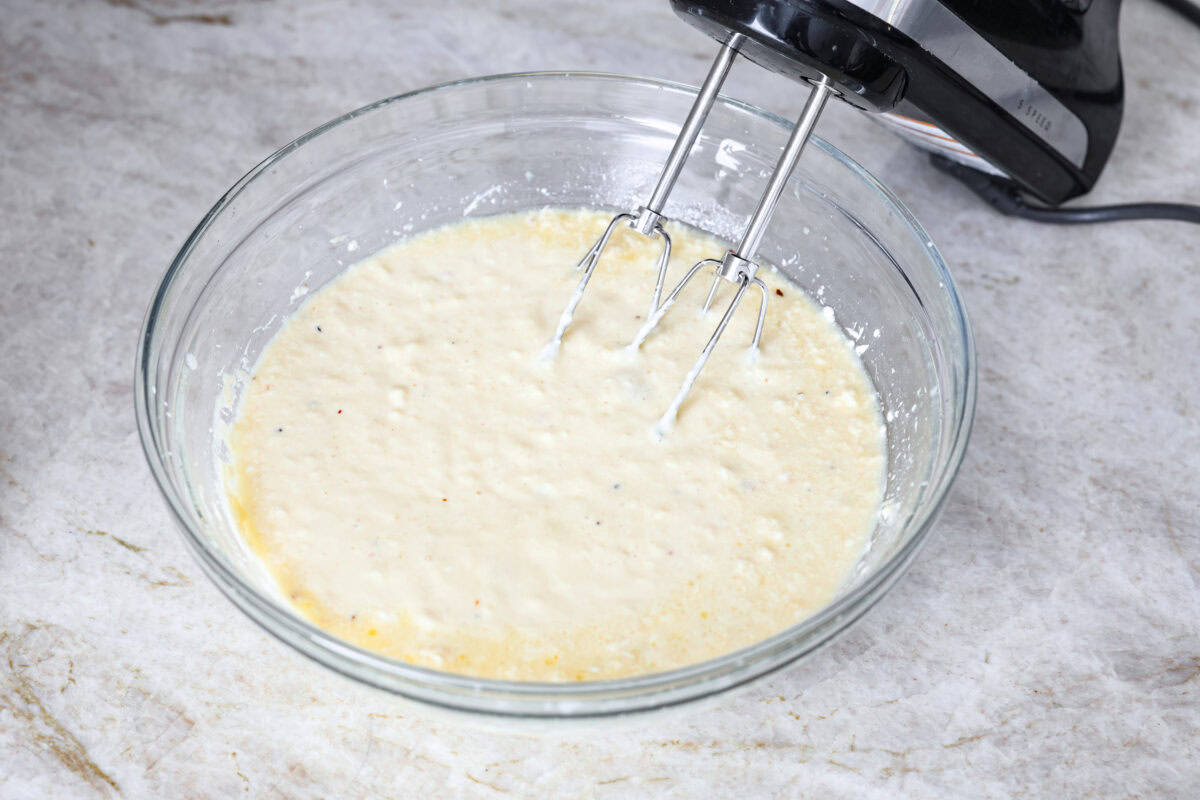 Angle shot of cream cheese, soup, butter, seasoning packet and chicken broth whisked together in a bowl with a hand mixer.