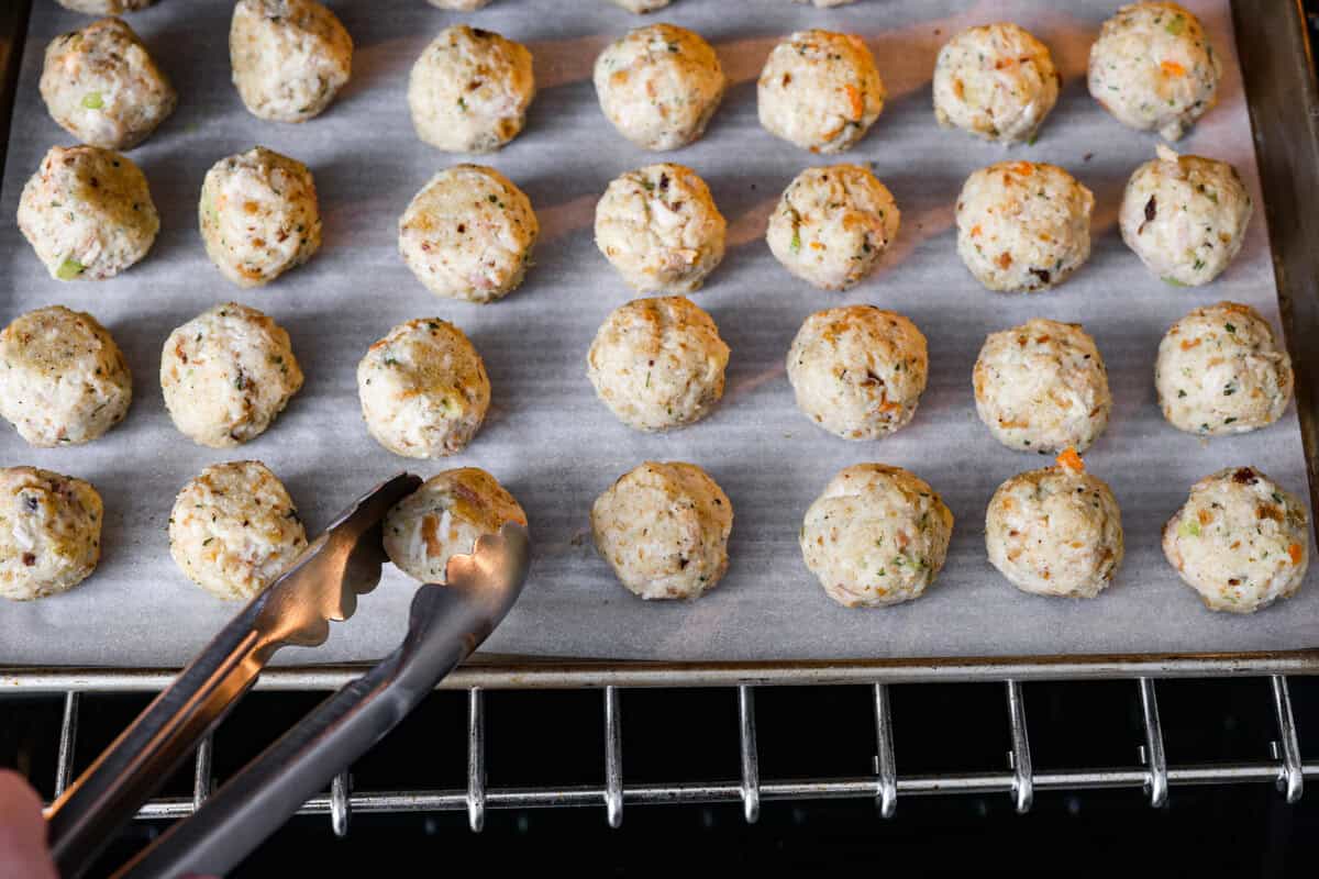 Turkey Stuffing Balls capture the taste of Thanksgiving in a single bite! Made with tender turkey, flavorful stuffing, and mashed potatoes. They’re rolled into perfectly poppable bites and served with rich gravy for dipping. Angle shot of someone flipping the balls in the oven.