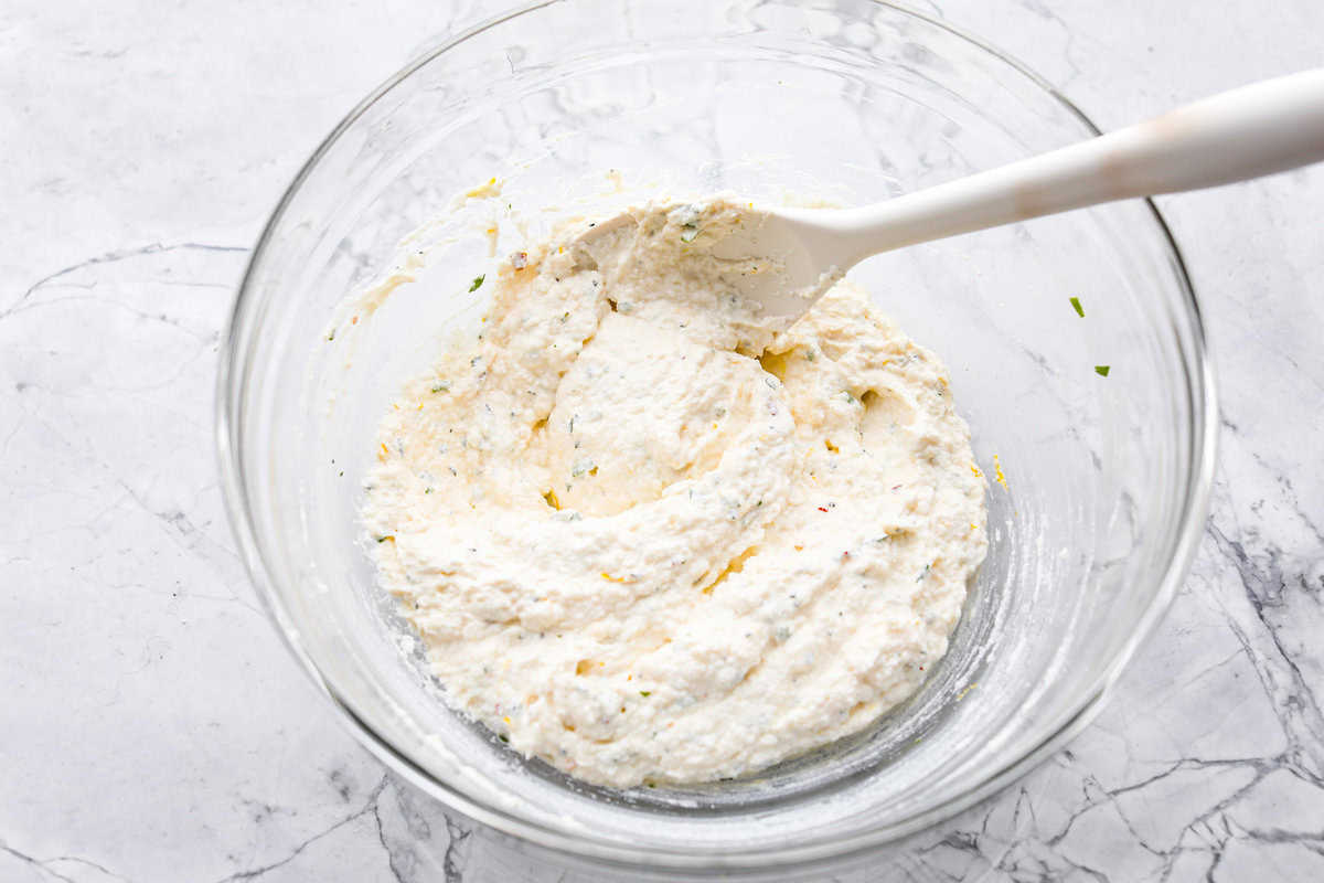 Irresistible Baked Ricotta Dip is the perfect party appetizer! It takes just minutes to combine creamy ricotta cheese with parmesan, fresh herbs, and lemon zest. Then, bake until bubbly and delicious, and get ready for an explosion of flavor! Overhead shot of ingredients stirred up in a glass bowl.