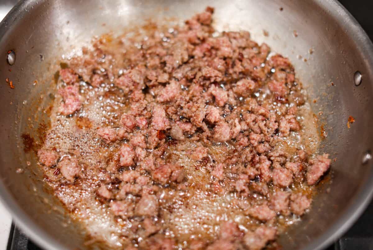 Overhead shot of the sausage being cooked in the bacon grease in a skillet. 