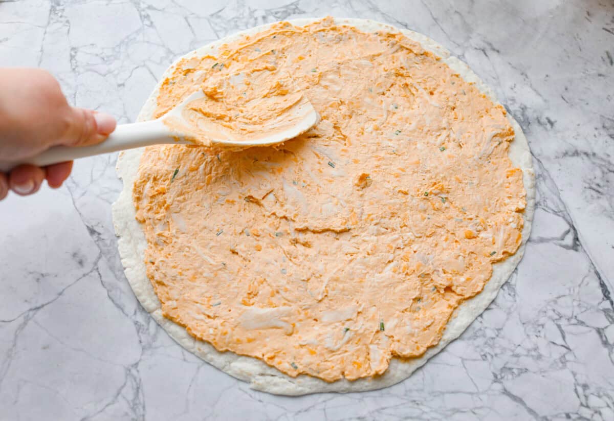 Fourth photo of the buffalo chicken mixture spreading onto a tortilla