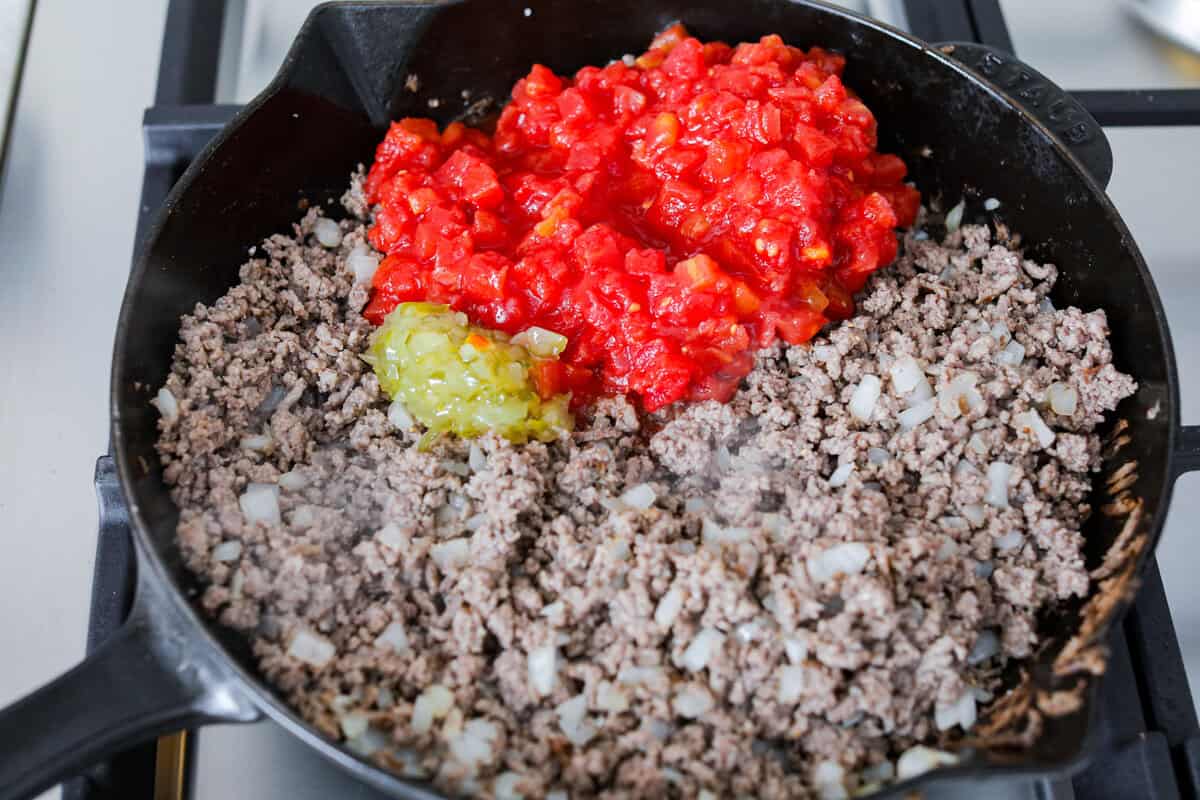 Cheeseburger dip is a crowd-pleasing appetizer for potlucks, parties, and get-togethers! This recipe takes delicious cheeseburger ingredients like beef, onion, tomato, relish, and cheese and turns them into a deliciously addicting snack! Overhead shot of browned beef with onions, tomatoes and relish.