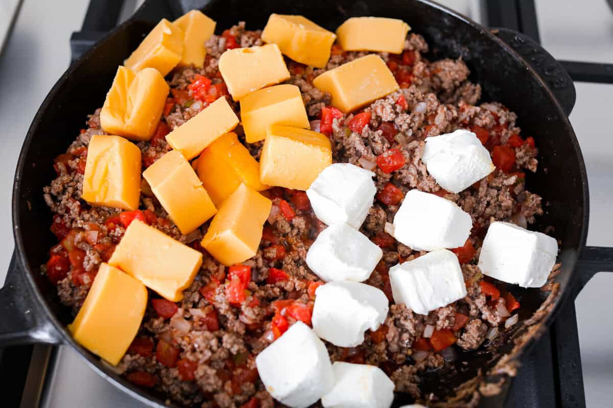 Cheeseburger dip is a crowd-pleasing appetizer for potlucks, parties, and get-togethers! This recipe takes delicious cheeseburger ingredients like beef, onion, tomato, relish, and cheese and turns them into a deliciously addicting snack! Overhead shot of beef mixture with Velveeta and cream cheese on top.