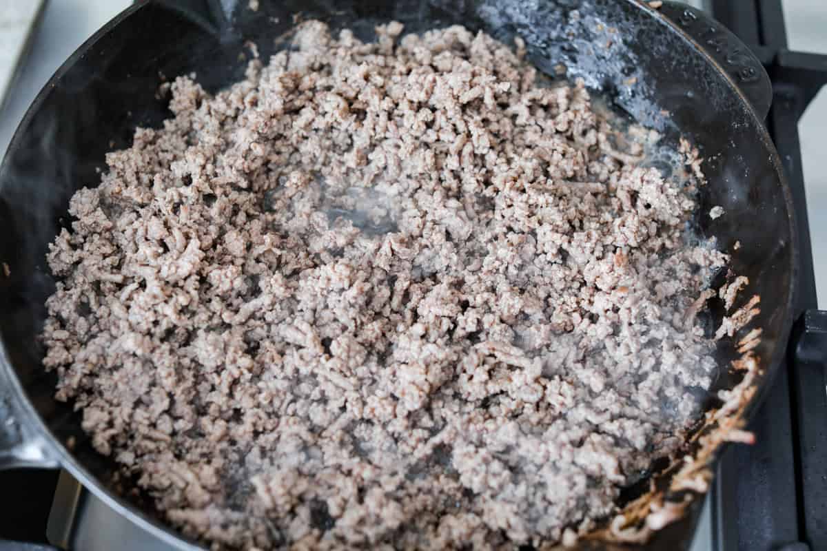 Cheeseburger dip is a crowd-pleasing appetizer for potlucks, parties, and get-togethers! This recipe takes delicious cheeseburger ingredients like beef, onion, tomato, relish, and cheese and turns them into a deliciously addicting snack! Overhead shot of beef being browned in a skillet.