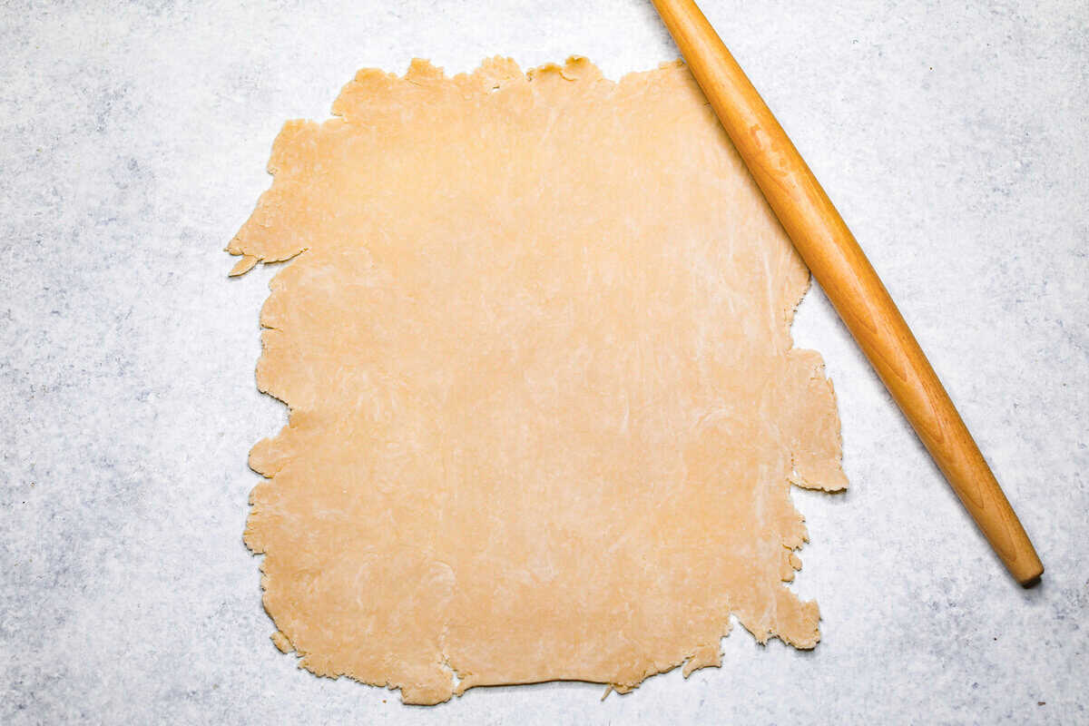 Cherry Slab Pie is an American classic made to serve a crowd! This recipe uses a tender, flaky crust that surrounds sweet, juicy cherry pie filling. It tastes incredibly delicious and is the perfect dessert for any time of year. Overhead shot of pie crust rolled into a rectangle with a rolling pin next to it.