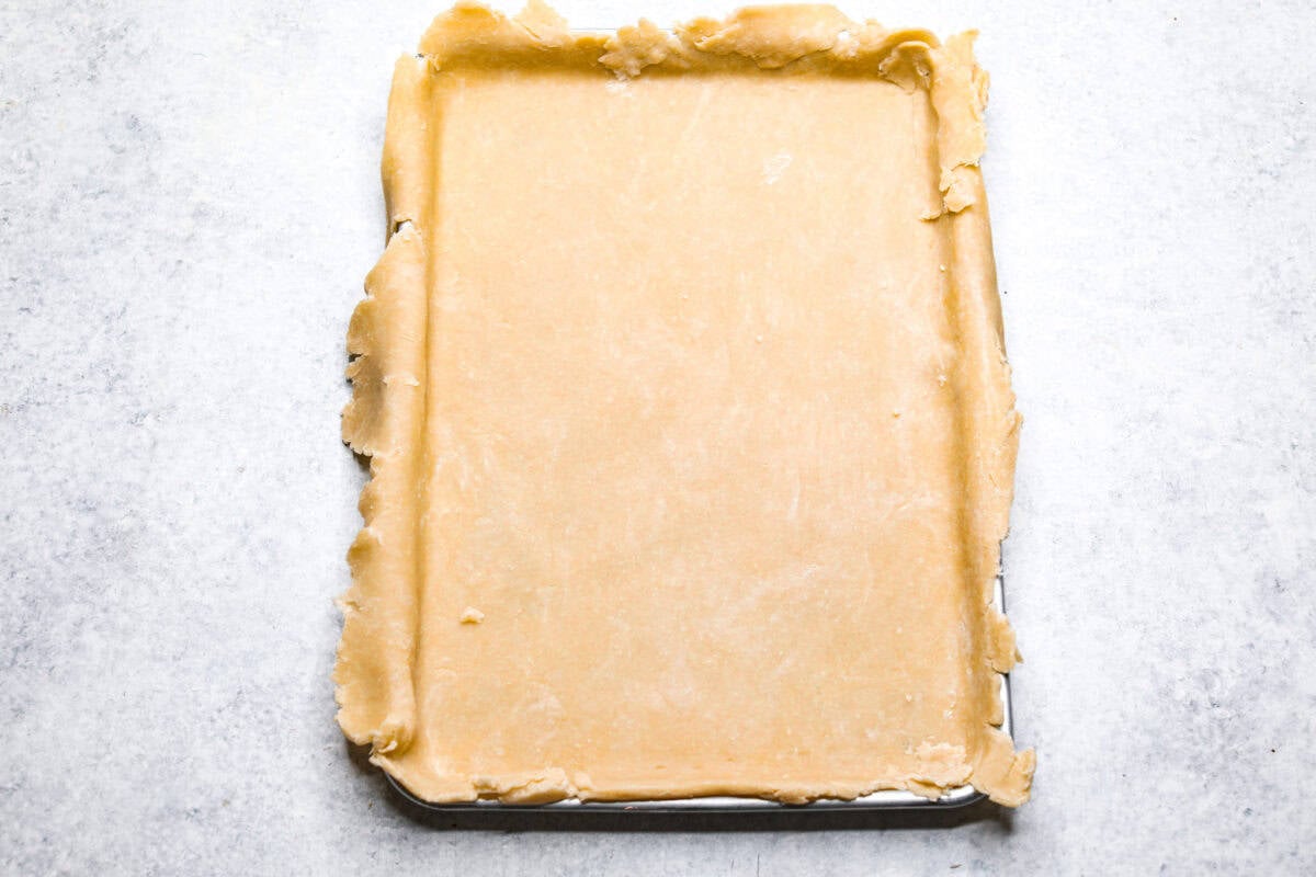 Overhead shot of pie crust spread out in jelly roll pan. 