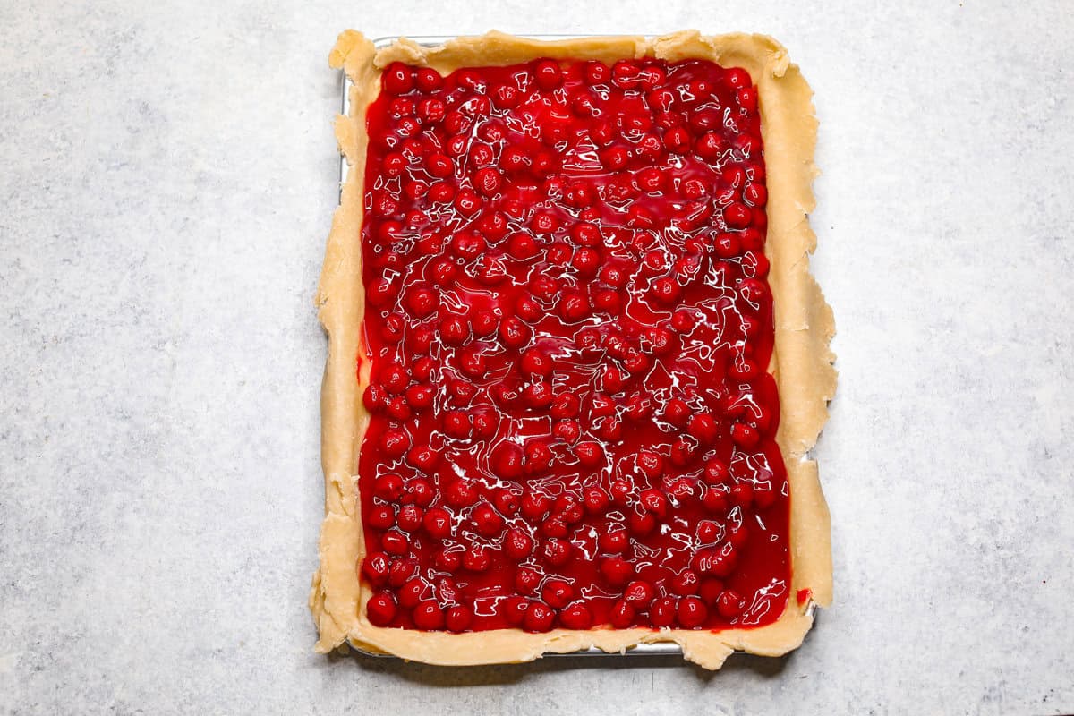 Cherry Slab Pie is an American classic made to serve a crowd! This recipe uses a tender, flaky crust that surrounds sweet, juicy cherry pie filling. It tastes incredibly delicious and is the perfect dessert for any time of year. Overhead shot of pie crust on sheet pan filled with cherry pie filling.