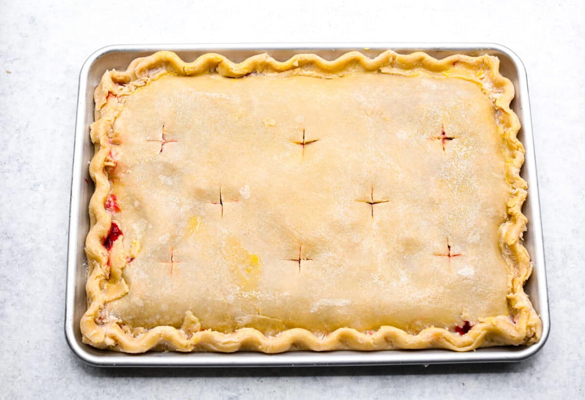 Overhead shot of cherry slab pie with cross shaped holes cut in to the top crust. 