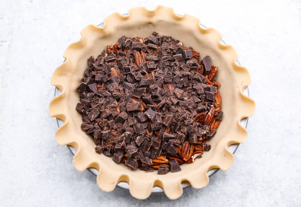 Overhead shot of a layer of chocolate chunks over the pecans in a pie crust. 