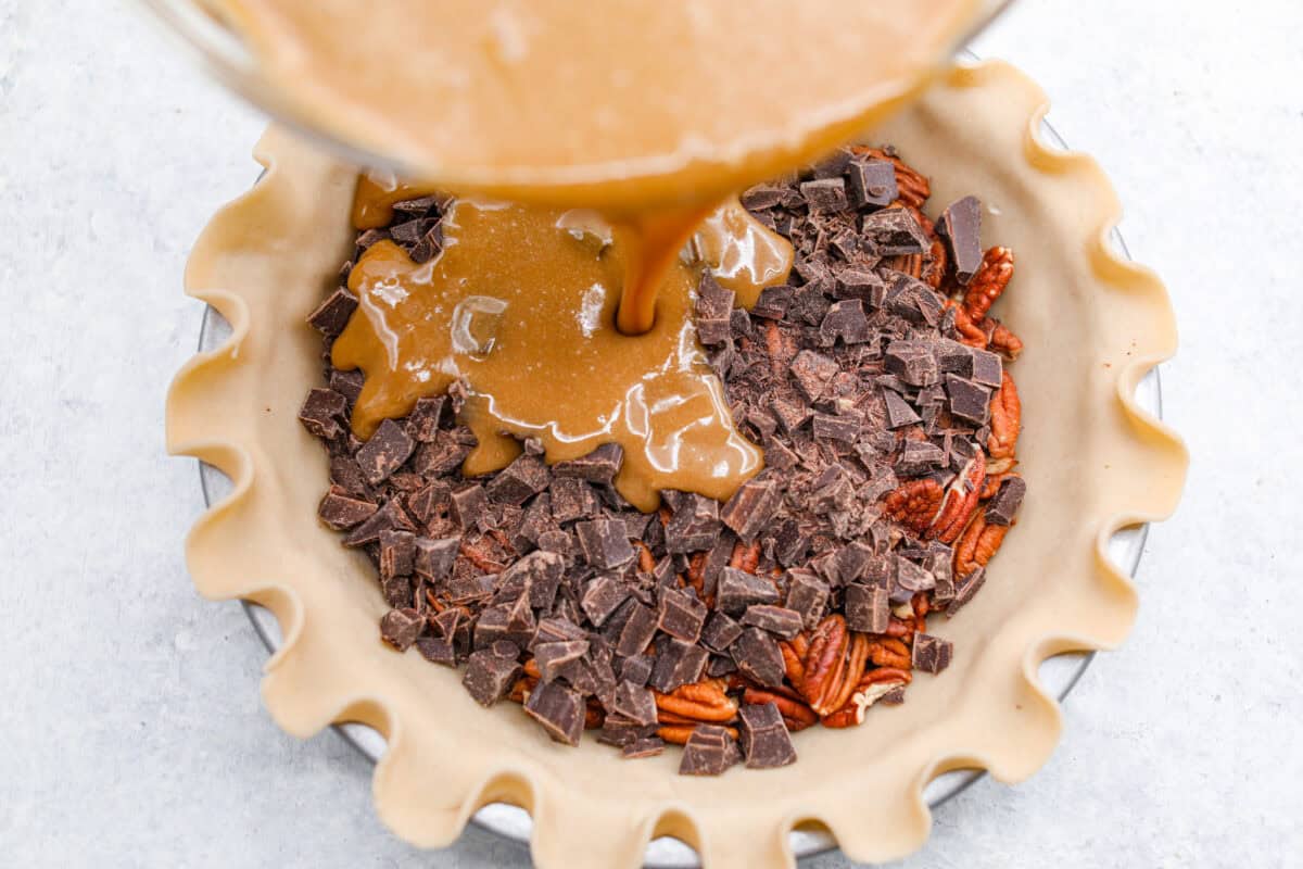 Overhead shot of someone pouring the egg, sugar and butter mixture over the chocolate and pecans in the pie crust. 