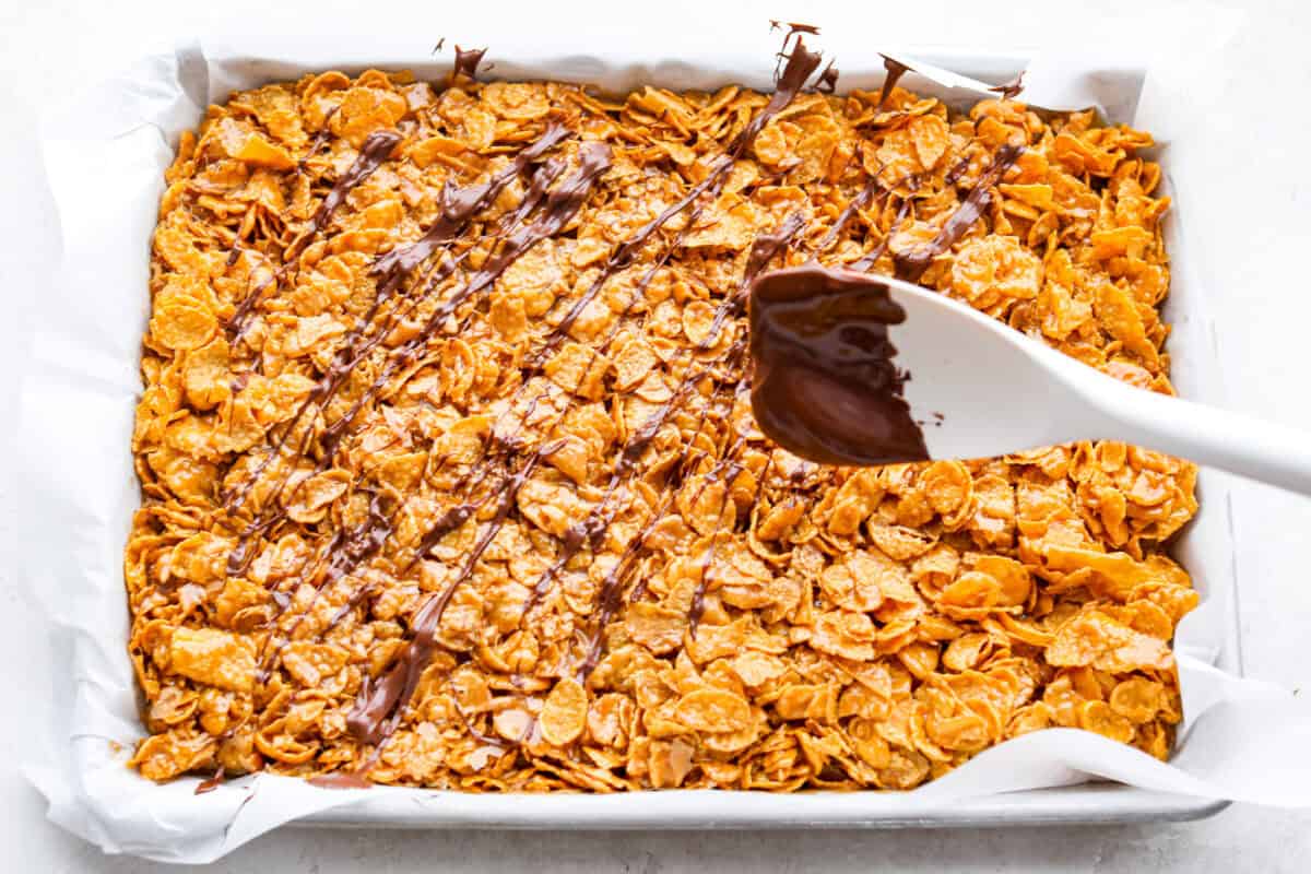 The photo from above shows someone drizzling chocolate over a mixture of cornflakes and caramel. 