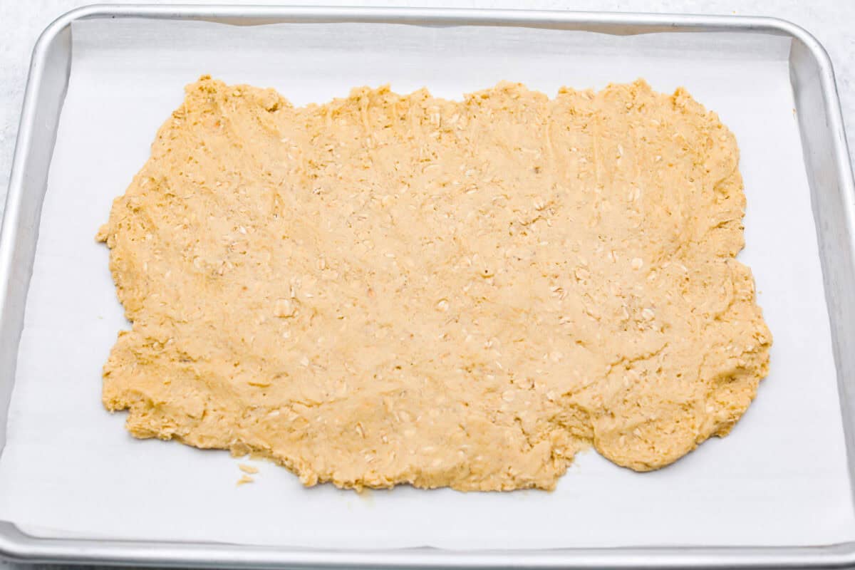 Overhead shot of oatmeal cookie dough smashed into a rectangle on parchment paper on a cookie sheet. 