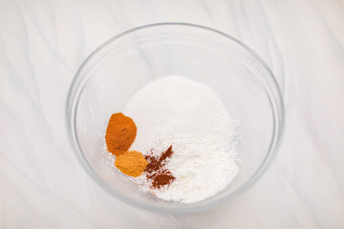 Crustless pumpkin pie has rich spices, creamy pumpkin, and a perfectly smooth texture. The custard holds its shape beautifully. Whether you're keeping things simple or exploring a gluten-free option, this pie gives all the nostalgic vibes of the classic. Overhead shot of dry ingredients in a glass bowl.