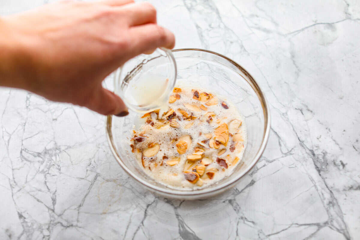 Green Beans Almondine is made with fresh green beans that are sautéed until crisp-tender and then tossed with buttery, toasted almonds. Every bite is filled with nutty richness and a hint of lemon to brighten up the flavors. Overhead shot of someone pouring lemon juice into a bowl of the butter and almonds.