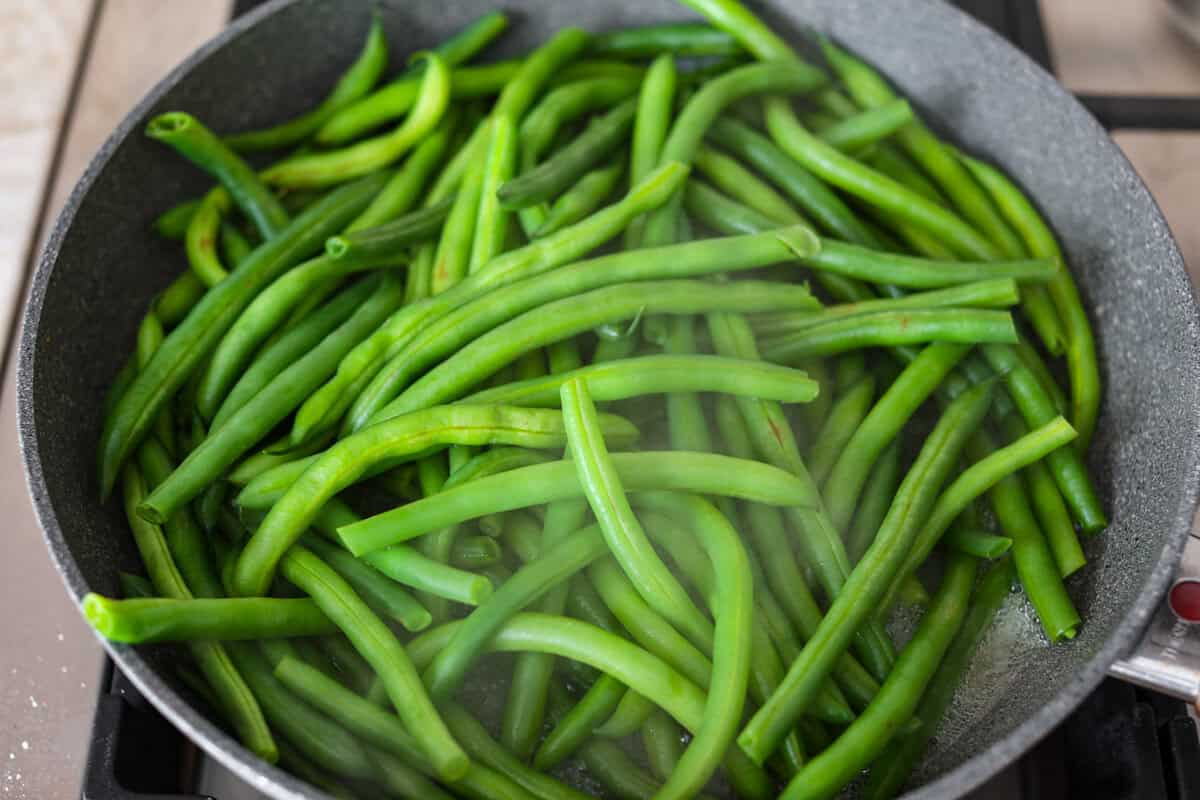 Green Beans Almondine is made with fresh green beans that are sautéed until crisp-tender and then tossed with buttery, toasted almonds. Every bite is filled with nutty richness and a hint of lemon to brighten up the flavors. Overhead shot of beans steaming in a skillet.