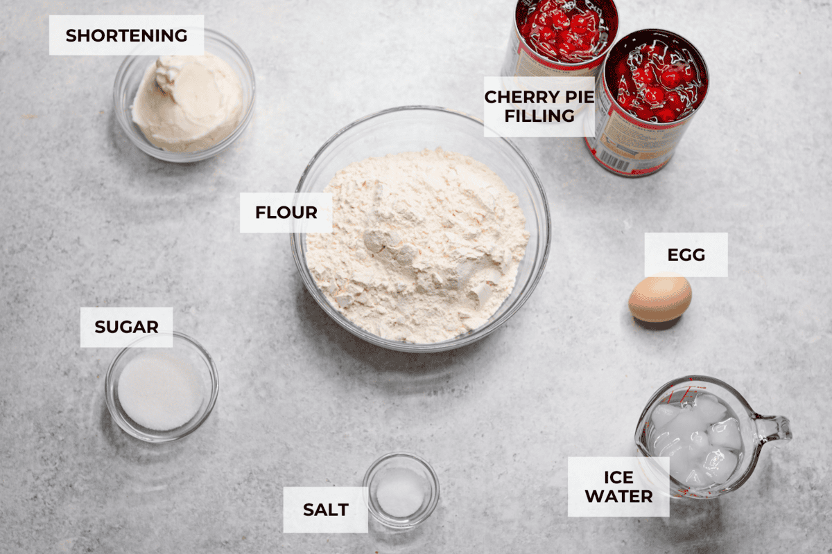 Cherry Slab Pie is an American classic made to serve a crowd! This recipe uses a tender, flaky crust that surrounds sweet, juicy cherry pie filling. It tastes incredibly delicious and is the perfect dessert for any time of year. Overhead shot of labeled ingredients.