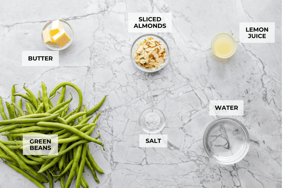 Green Beans Almondine is made with fresh green beans that are sautéed until crisp-tender and then tossed with buttery, toasted almonds. Every bite is filled with nutty richness and a hint of lemon to brighten up the flavors. Overhead shot of labeled ingredients.