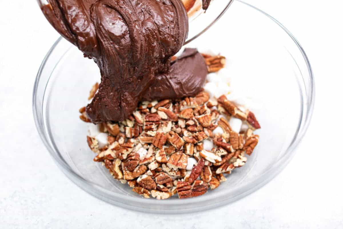 Angle shot of someone pouring the chocolate mixture into the nuts and marshmallows. 