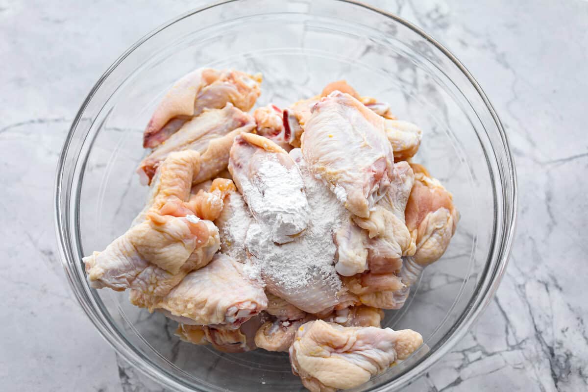 These sweet and sour wings are the perfect appetizer to serve for your next party, game day, or after-school snack. They are baked to crispy perfection and then doused in a sticky, sweet, and sour sauce. Overhead shot of raw wings with baking powder in a glass bowl.