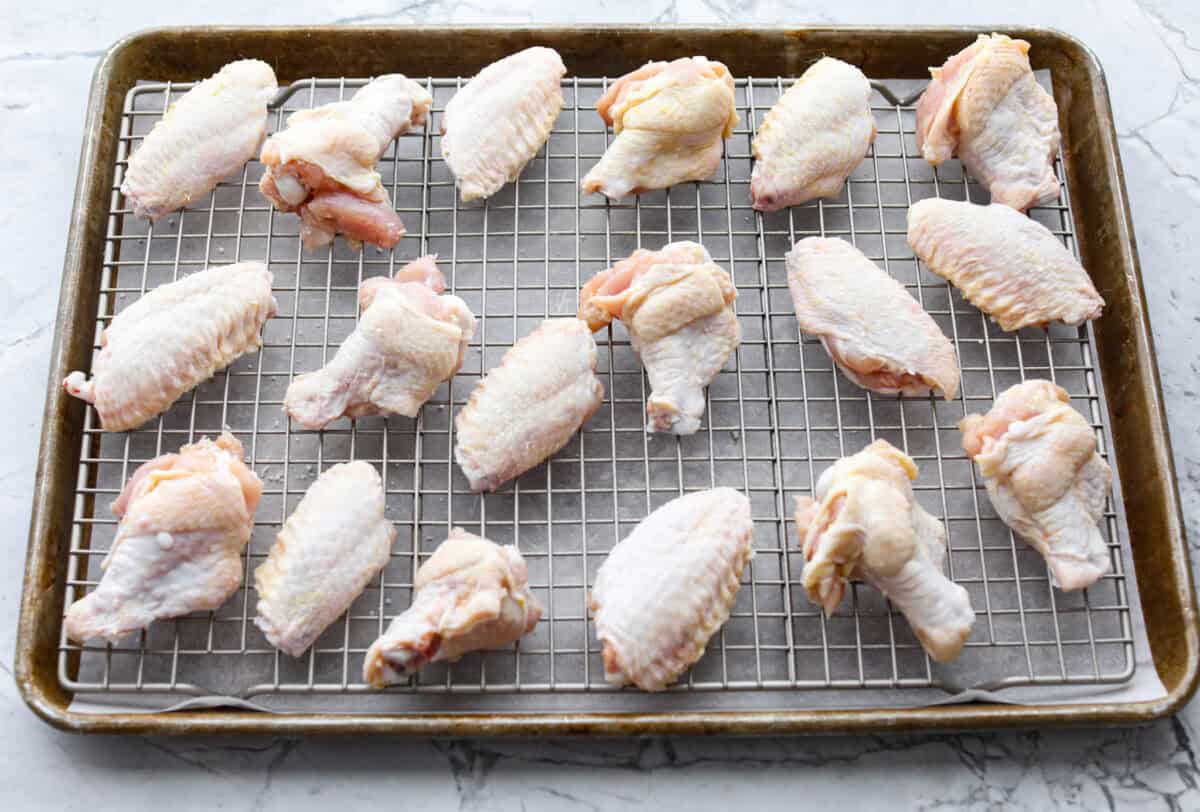 Raw wings on a baking rack over parchment paper on a cookie sheet. 