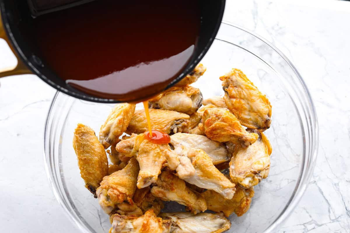 These sweet and sour wings are the perfect appetizer to serve for your next party, game day, or after-school snack. They are baked to crispy perfection and then doused in a sticky, sweet, and sour sauce. Angle shot of someone pouring sweet and sour sauce over baked chicken wings.
