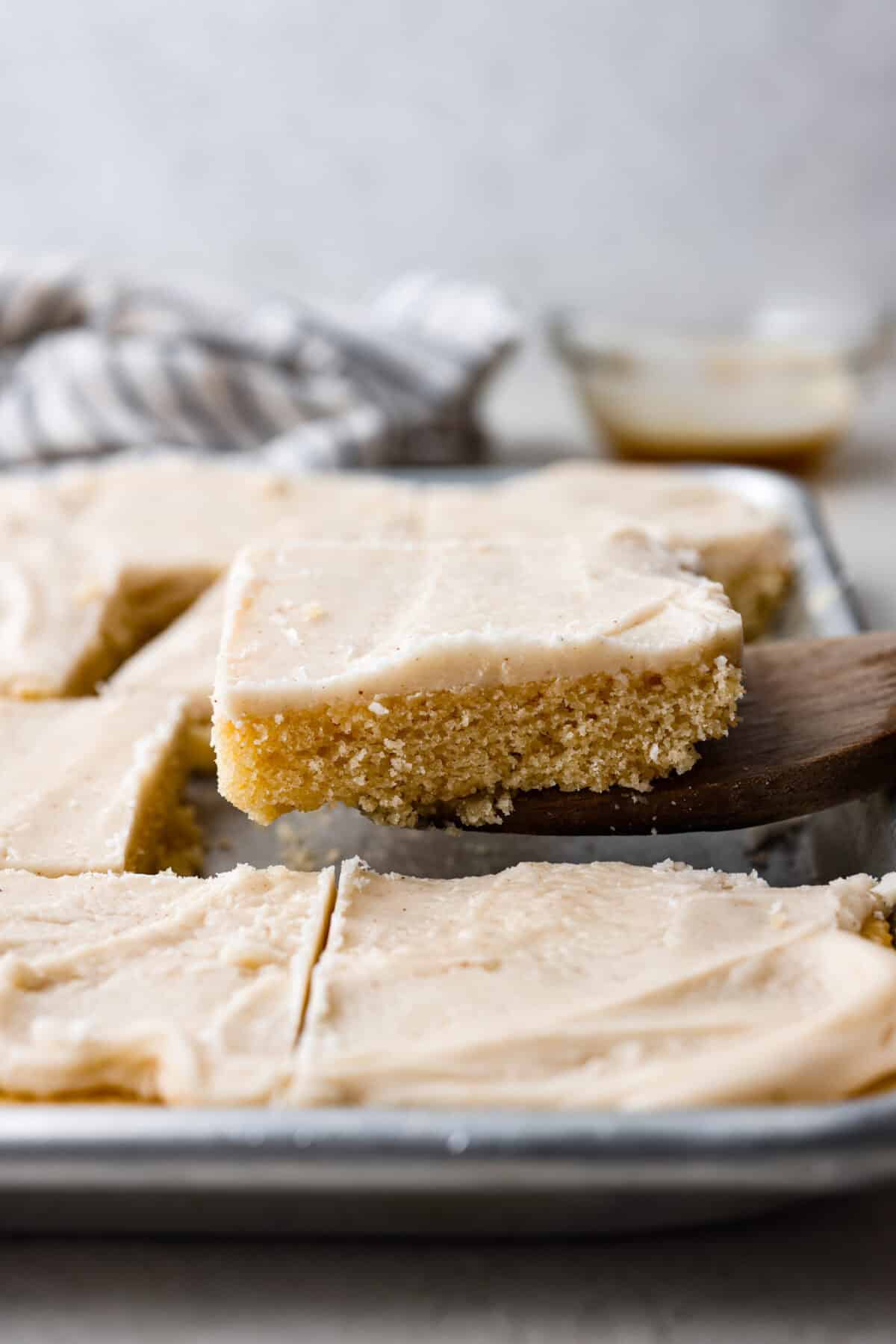 Side shot of someone lifting a slice of browned butter sheet cake out of the pan. 