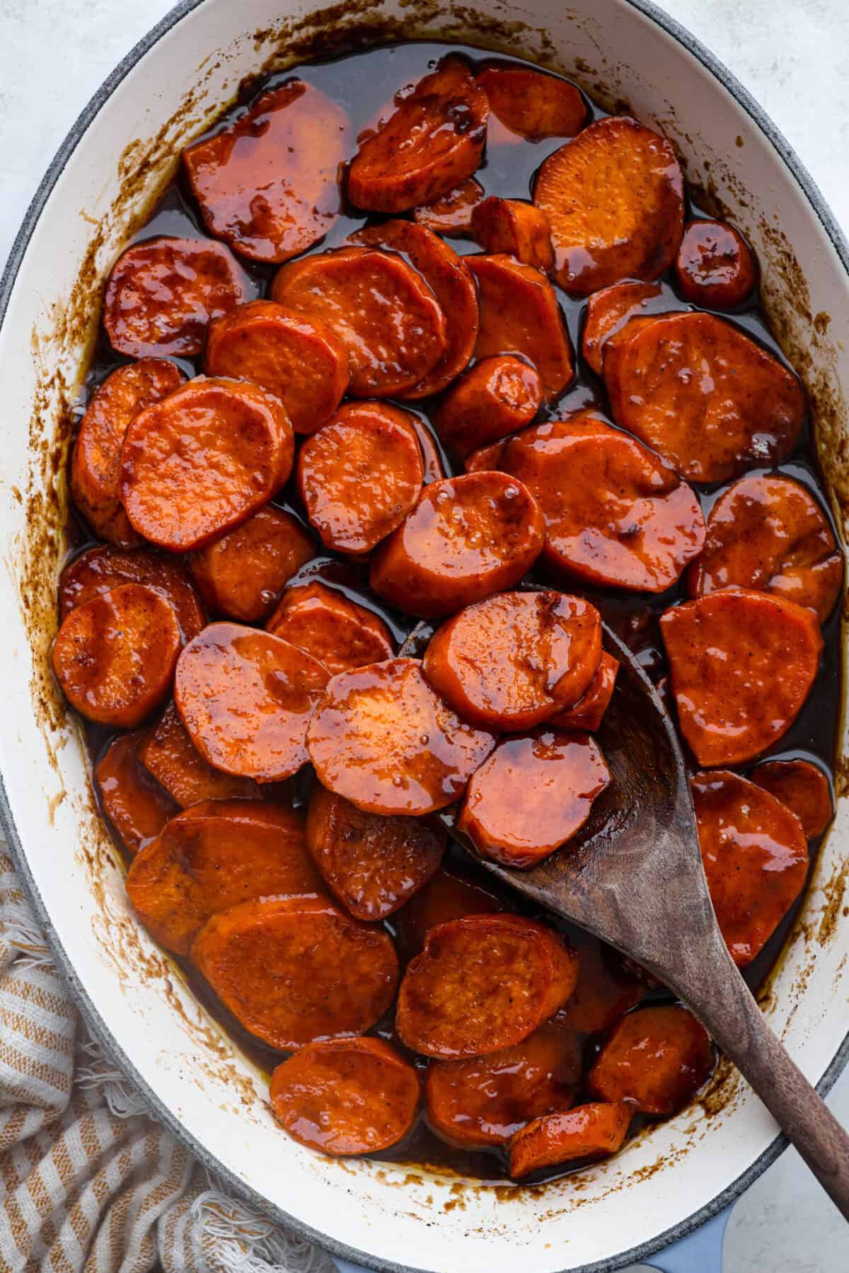 Overhead shot of baked candied yams in a baking dish with a wooden serving spoon. 