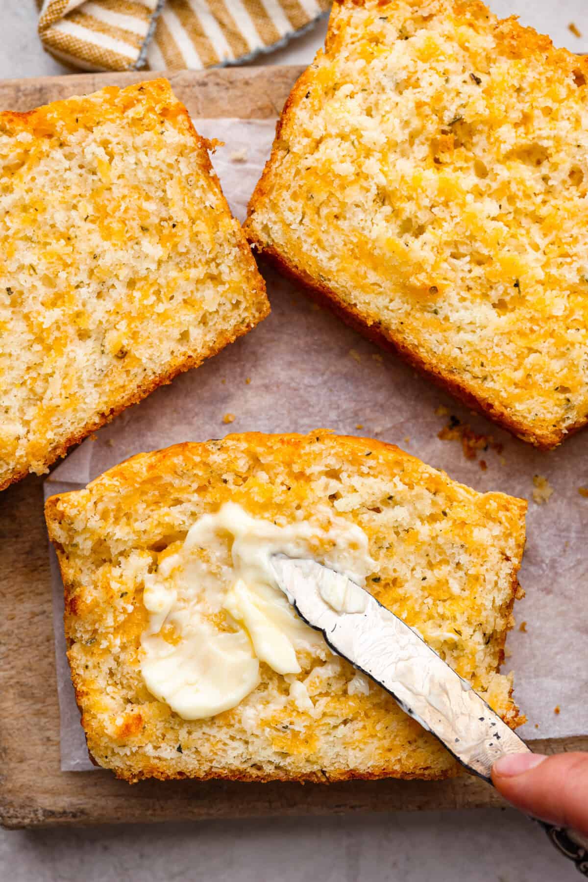 Close up shot of someone spreading butter on a slice of cheesy quick bread. 